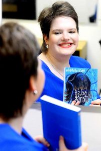 A képen Kováts Laura Rozális látható. Könyvet tart a kezében egy tükör előtt.